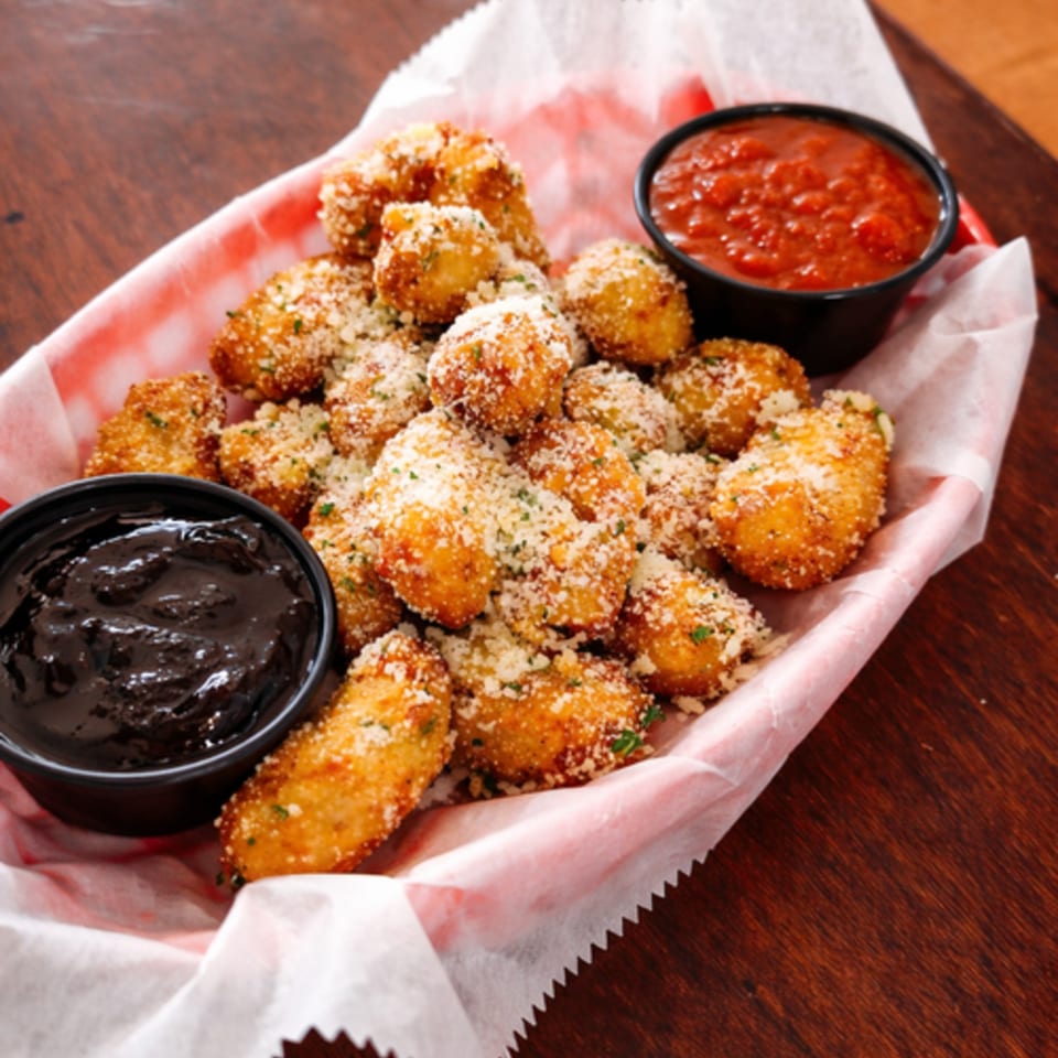 A basket of golden-brown fried cheese curds, sprinkled with parmesan and parsley, with two dipping sauces.