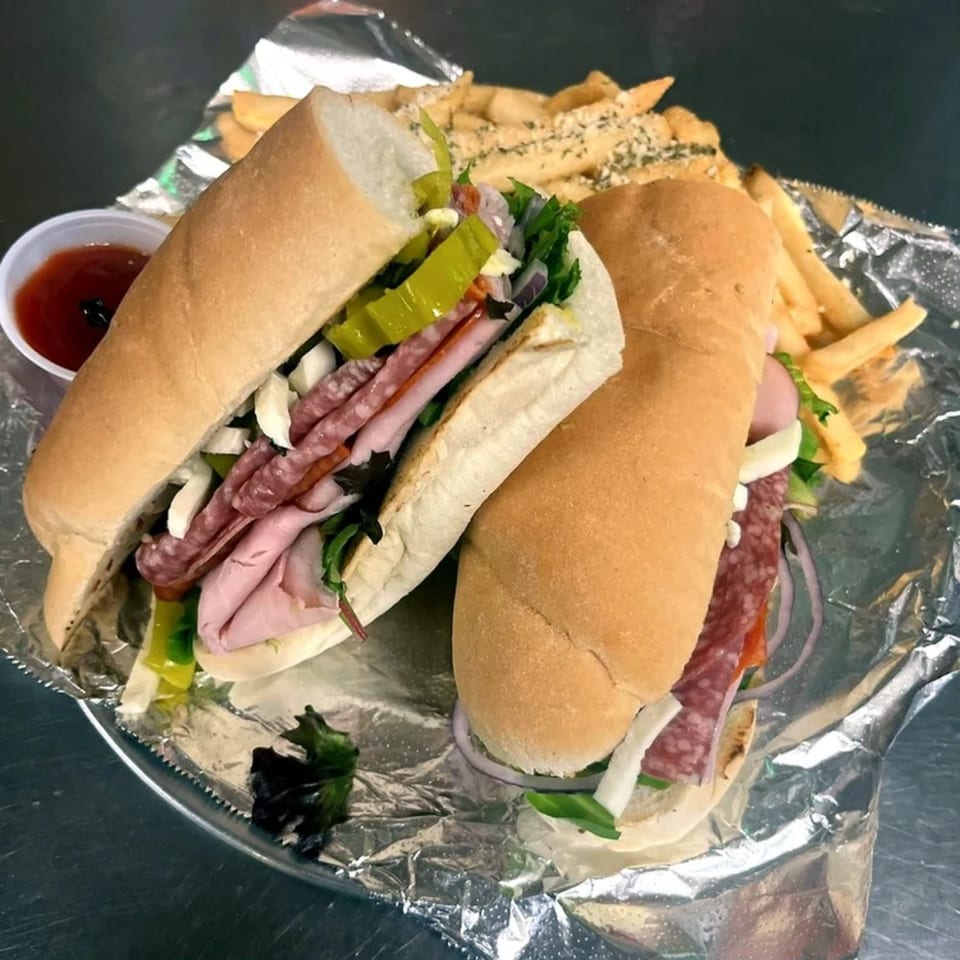 Two deli subs with various meats, cheese, and vegetables, served with fries and ketchup.