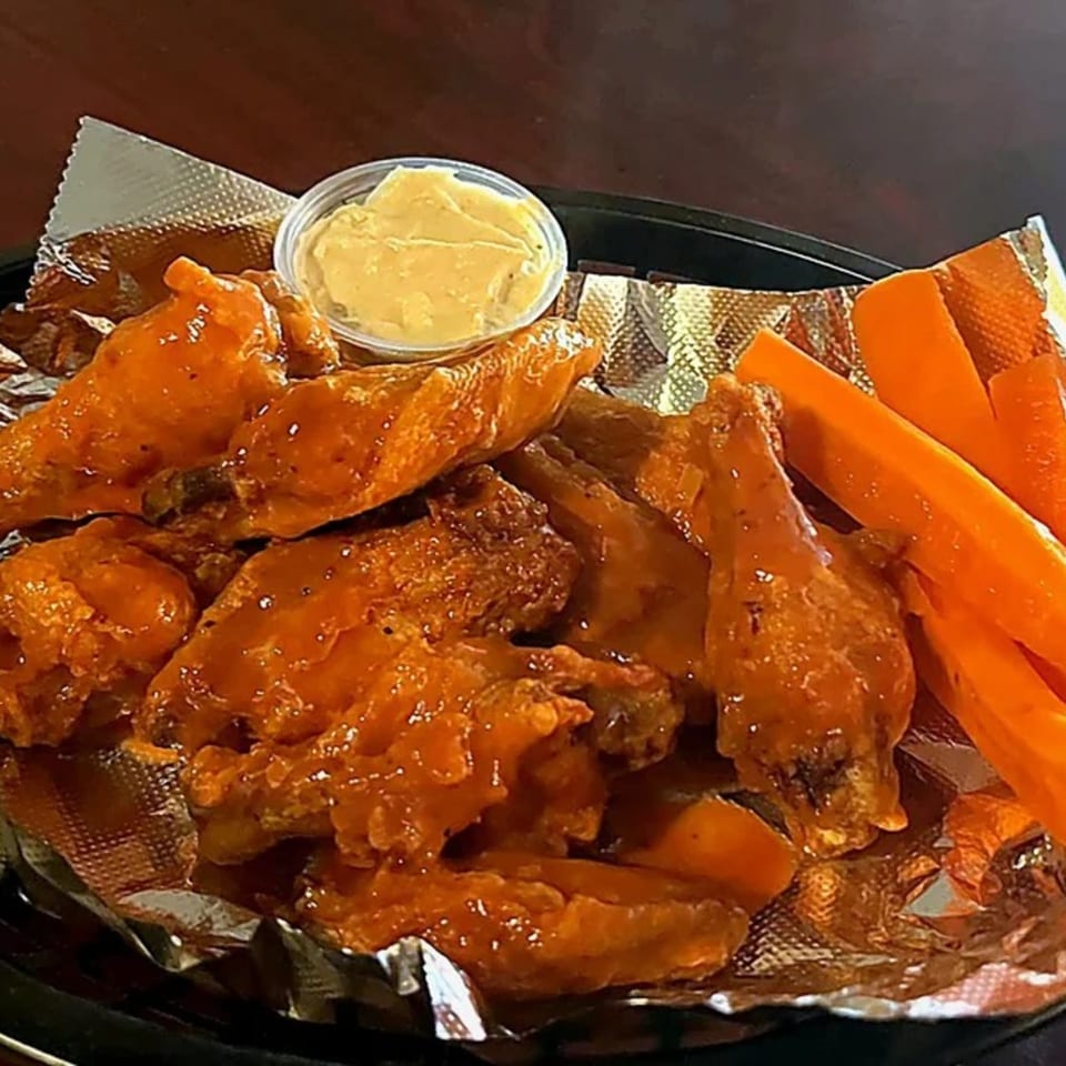 A platter of buffalo wings with a side of carrot sticks and a small cup of dipping sauce.